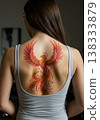Rear View Of A Young Woman With A Colorful Phoenix Tattoo On Her Back In A Bright Room 138333879