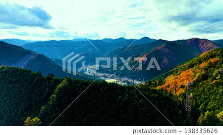 A drone shot of a peaceful town surrounded by mountains, sky, and autumn foliage. A drone shot of a peaceful town surrounded by mountains, sky, and autumn foliage. 138335626