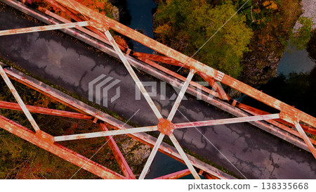 A drone aerial shot of a red bridge spanning a valley amidst autumn foliage. 138335668