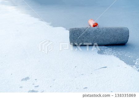 Close-up of a paint roller applying white liquid coating or sealant on a grey industrial floor. Construction site floor renovation and waterproofing process. Space for text on the surface. Close-up of a paint roller applying white liquid coating or sealant on a grey industrial floor. Construction site floor renovation and waterproofing process. Space for text on the surface. 138335869