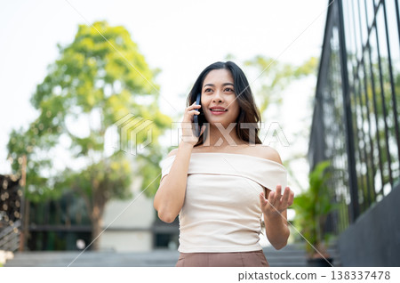Pretty asian woman open palm as talking on phone call while standing walking on stairs by building. 138337478
