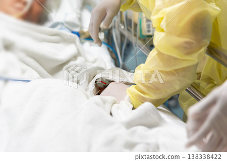 Healthcare worker in protective gown assisting patient in hospital bed with medical monitoring equipment showing clinical care treatment support and recovery in modern hospital environment Healthcare worker in protective gown assisting patient in hospital bed with medical monitoring equipment showing clinical care treatment support and recovery in modern hospital environment 138338422