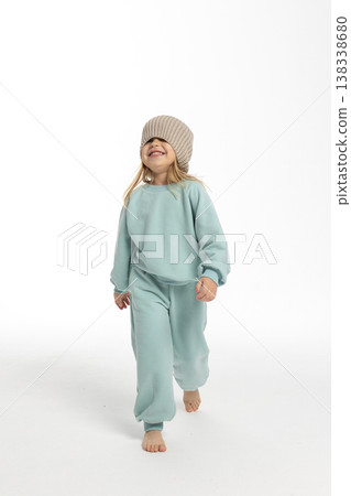 Portrait of beautiful cute little toddler girl. Child with funny face in mint sweatshirt and hat. Pretty smile kid in studio on white background. 138338680