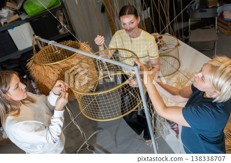 Guiding instructor demonstrating weaving technique while participants assemble decorative chandelier frames with cords in studio. 138338707