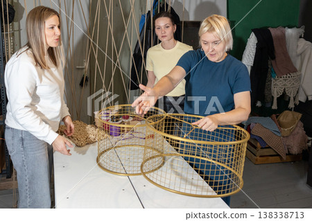 Guiding instructor demonstrating weaving technique while participants assemble decorative chandelier frames with cords in studio. 138338713