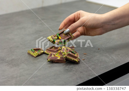 Woman's hand holds piece of Dubai chocolate on gray background. Green kadayif and pistachio spread with pistachio in trend dessert. Close-up, selective focus. High quality photo Woman's hand holds piece of Dubai chocolate on gray background. Green kadayif and pistachio spread with pistachio in trend dessert. Close-up, selective focus. High quality photo 138338747