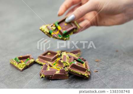 Woman's hand holds piece of Dubai chocolate on gray background. Green kadayif and pistachio spread with pistachio in trend dessert. Close-up, selective focus. High quality photo Woman's hand holds piece of Dubai chocolate on gray background. Green kadayif and pistachio spread with pistachio in trend dessert. Close-up, selective focus. High quality photo 138338748