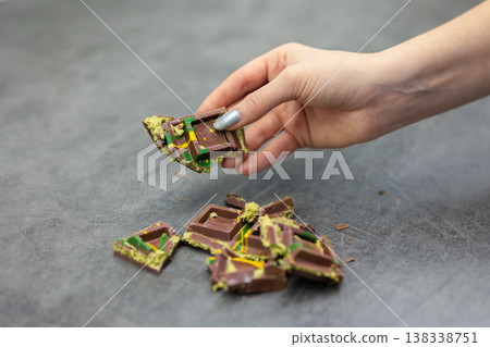 Woman's hand holds piece of Dubai chocolate on gray background. Green kadayif and pistachio spread with pistachio in trend dessert. Close-up, selective focus. High quality photo Woman's hand holds piece of Dubai chocolate on gray background. Green kadayif and pistachio spread with pistachio in trend dessert. Close-up, selective focus. High quality photo 138338751