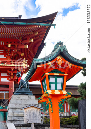 Fushimi Inari Shrine with Fox statue with red bib and symbolic key seated on stone pedestal against blue sky, Japan Fushimi Inari Shrine with Fox statue with red bib and symbolic key seated on stone pedestal against blue sky, Japan 138338772