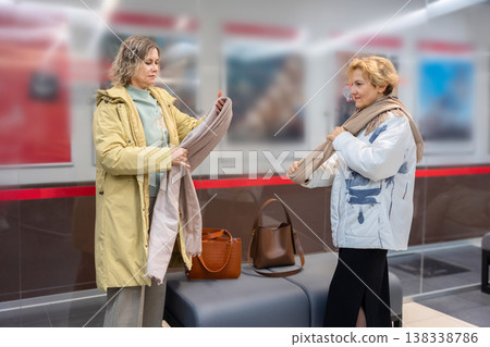 Female visitors removing warm clothing in interior lobby space near hangers and storage preparing for event or meeting. Female visitors removing warm clothing in interior lobby space near hangers and storage preparing for event or meeting. 138338786
