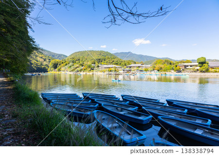 Traditional wooden boats moored on calm river under large tree in Kyoto with Togetsukyo bridge in background, Japan  138338794