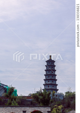 Multi tier pagoda rising above green trees and rooftops under pale sky within historic Gubei Water Town China. Multi tier pagoda rising above green trees and rooftops under pale sky within historic Gubei Water Town China. 138338821