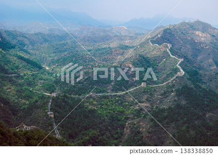 Historic of Great Wall fortification lines rugged terrain with winding path descending toward watchtowers emphasizing scale of ancient structure, Simatai, Beijing, China 138338850