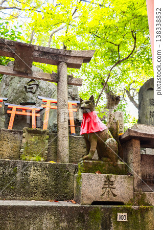 Fox statue with red bib and symbolic key seated on stone pedestal at Fushimi Inari Shrine in Kyoto, Japan 138338852