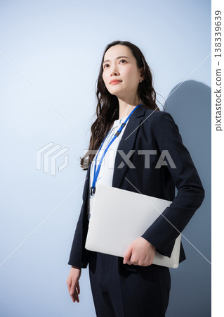 一位身著職業套裝、佩戴名牌、手持筆記型電腦的干練女性,背景是淺藍色。畫面中,她正仰望著未來和目標。 一位身著職業套裝、佩戴名牌、手持筆記型電腦的干練女性,背景是淺藍色。畫面中,她正仰望著未來和目標。 138339639
