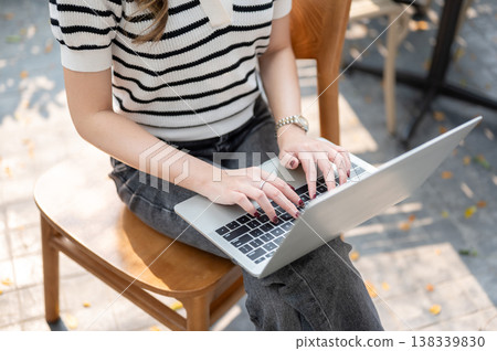 Close up of woman's manicured hands typing on laptop as sitting on wooden chair over pavement ground Close up of woman's manicured hands typing on laptop as sitting on wooden chair over pavement ground 138339830