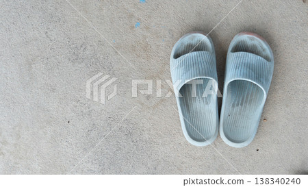 Top view of a pair of used light blue rubber slides or slippers placed on a textured grey concrete floor with copy space. 138340240