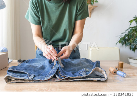 Woman's hands sewing denim jeans, embracing craft, sustainability, and upcycling fashion on a wooden table. Reusing things. Environmental awareness 138341925