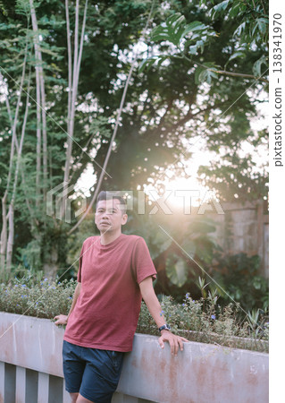 Southeast Asian man standing on bridge wearing red t-shirt looking at camera Southeast Asian man standing on bridge wearing red t-shirt looking at camera 138341970
