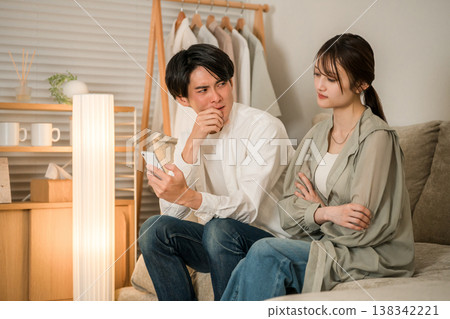 A young Asian couple is looking at their smartphones on the living room sofa, troubled and worried. A young Asian couple is looking at their smartphones on the living room sofa, troubled and worried. 138342221