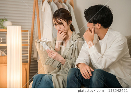 A young Asian couple is looking at their smartphones on the living room sofa, troubled and worried. A young Asian couple is looking at their smartphones on the living room sofa, troubled and worried. 138342431