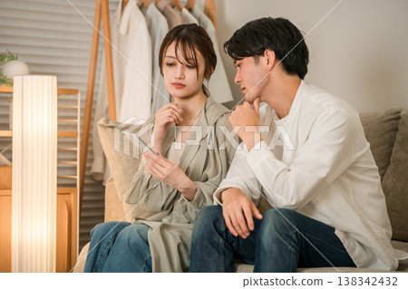 A young Asian couple is looking at their smartphones on the living room sofa, troubled and worried. 138342432
