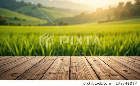 Rustic wooden tabletop foreground with a blurred background of rolling green hills and a lush field under a warm morning sun. 138342887