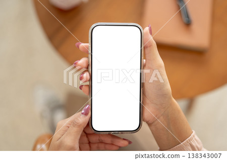 Close up of a woman's manicured hands holding blank screen phone and sitting at wooden table in cafe Close up of a woman's manicured hands holding blank screen phone and sitting at wooden table in cafe 138343007