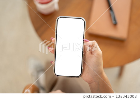 Close up of a woman's manicured hand holding white screen smartphone sitting at wooden table in cafe Close up of a woman's manicured hand holding white screen smartphone sitting at wooden table in cafe 138343008