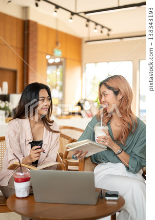 Asian woman student drinking milk tea and talking to a friend while working on group project in cafe Asian woman student drinking milk tea and talking to a friend while working on group project in cafe 138343193