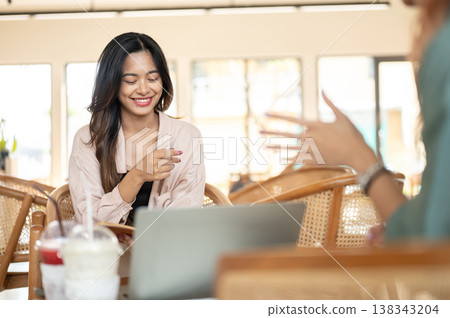 Asian woman student smiling at her friend while working on group project or study together in cafe. Asian woman student smiling at her friend while working on group project or study together in cafe. 138343204