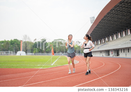 Athletic asian woman friends talking as running or jogging together on racetrack in sports stadium. Athletic asian woman friends talking as running or jogging together on racetrack in sports stadium. 138343216