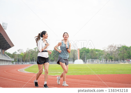 Athletic asian women friends in sportswear talking while running or jogging on racetrack in stadium. 138343218