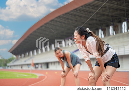 Asian woman and friend standing with hands on knees resting after running on track in sports stadium Asian woman and friend standing with hands on knees resting after running on track in sports stadium 138343232