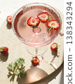 Pink strawberry margarita cocktail with sugar rim on marble tray. Fresh halved berries floating in sparkling rose drink with ice and sunlight shadows for summer party lifestyle. 138343294