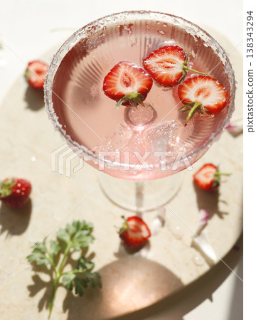 Pink strawberry margarita cocktail with sugar rim on marble tray. Fresh halved berries floating in sparkling rose drink with ice and sunlight shadows for summer party lifestyle. Pink strawberry margarita cocktail with sugar rim on marble tray. Fresh halved berries floating in sparkling rose drink with ice and sunlight shadows for summer party lifestyle. 138343294