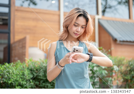 Asian woman in sportswear holding phone checking watch time preparing to go exercise at gym fitness. 138343547