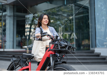 Pretty asian woman walking with a fat tire electric bicycle in front of a shopping mall or building. Pretty asian woman walking with a fat tire electric bicycle in front of a shopping mall or building. 138343701
