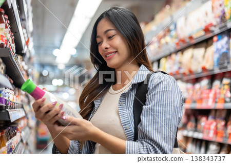 Pretty asian woman looking at sauce standing aside shelf as shopping in supermarket or grocery store 138343737