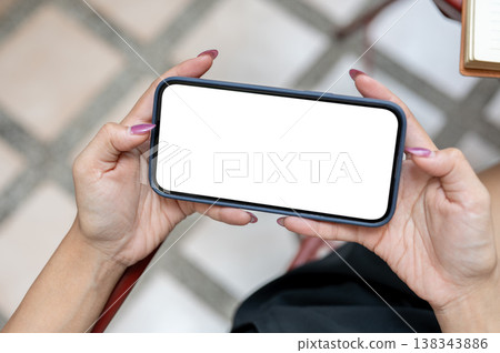 Top view of a woman's hands holding white screen phone watching video playing game at outdoor table. Top view of a woman's hands holding white screen phone watching video playing game at outdoor table. 138343886