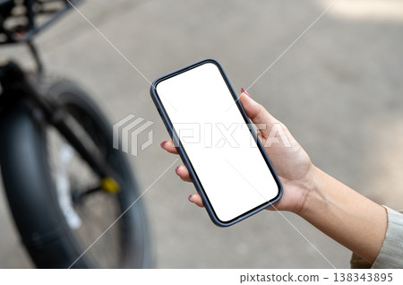 Top view of woman's hand holding white screen smartphone standing on street or pavement with bicycle Top view of woman's hand holding white screen smartphone standing on street or pavement with bicycle 138343895