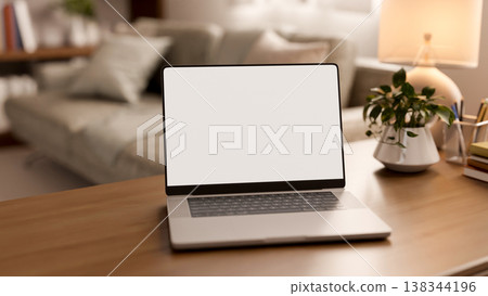 White screen laptop with pot plant and lamp on wooden table across sofa and bookshelf in living room White screen laptop with pot plant and lamp on wooden table across sofa and bookshelf in living room 138344196