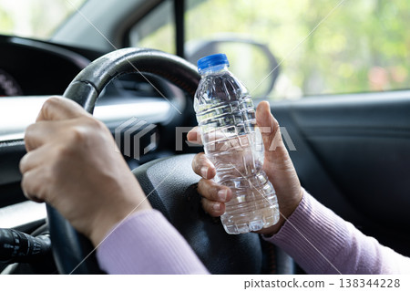 Asian woman driver holding bottle for drink water while driving a car. Plastic hot water bottle cause fire. Asian woman driver holding bottle for drink water while driving a car. Plastic hot water bottle cause fire. 138344228