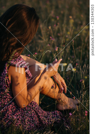 Beautiful girl in hat sitting on a flower meadow at sunset Beautiful girl in hat sitting on a flower meadow at sunset 138344303