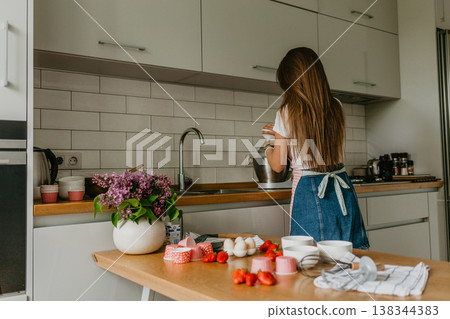 Young woman with confectionery bag squeezing cream on cupcakes 138344383