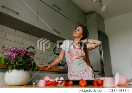 Happy baking cooking woman standing in her new kitchen smiling cheerful wearing apron and oven mitts ready to bake. Beautiful young mixed race Caucasian Chinese woman at home. Happy baking cooking woman standing in her new kitchen smiling cheerful wearing apron and oven mitts ready to bake. Beautiful young mixed race Caucasian Chinese woman at home. 138344384
