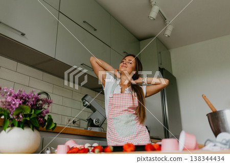 Happy baking cooking woman standing in her new kitchen smiling cheerful wearing apron and oven mitts ready to bake. Beautiful young mixed race Caucasian Chinese woman at home. 138344434