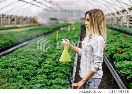 Portrait of smiling female florist watering plants in greenhouse. Portrait of smiling female florist watering plants in greenhouse. 138344588