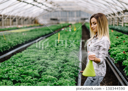 Portrait of smiling female florist watering plants in greenhouse. Portrait of smiling female florist watering plants in greenhouse. 138344590