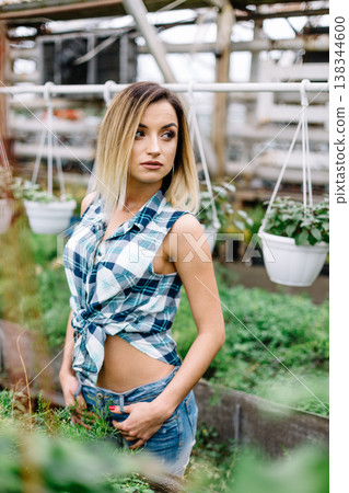 girl in long cardigan in plant shop chooses between two pots of pink flowers. Portrait of joyful lady in botanical garden. girl in long cardigan in plant shop chooses between two pots of pink flowers. Portrait of joyful lady in botanical garden. 138344600